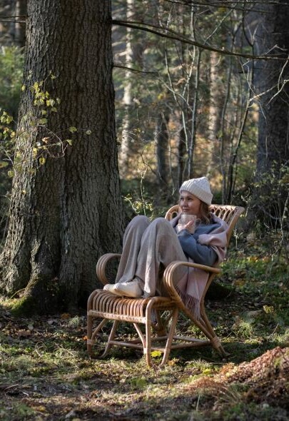 Nainen istuu Vintagetuolissa pipo päässä metsässä