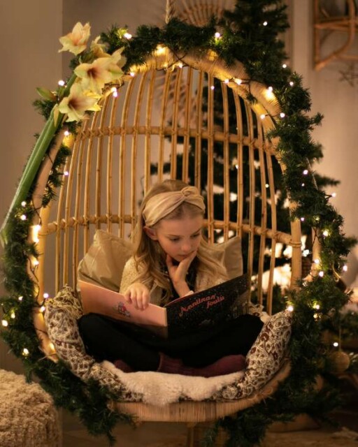 Sirkka riippukeinu on koristeltu jouluun, tyttö lukee kirjaa