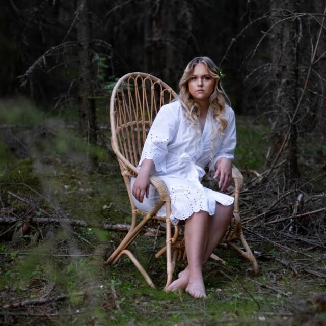 Nainen istuu Korkeassa lumikenkä tuolissa metsän siimeksessä