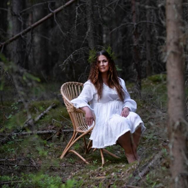 Nainen istuu matalassa lumikenkä tuolissa metsässä
