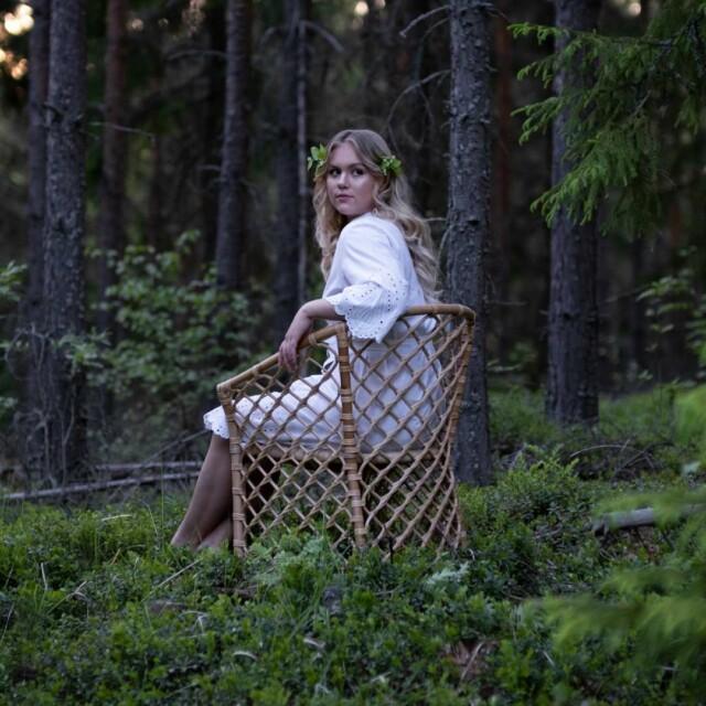 Nainen istuu Marina rottinkituolissa keskellä metsää