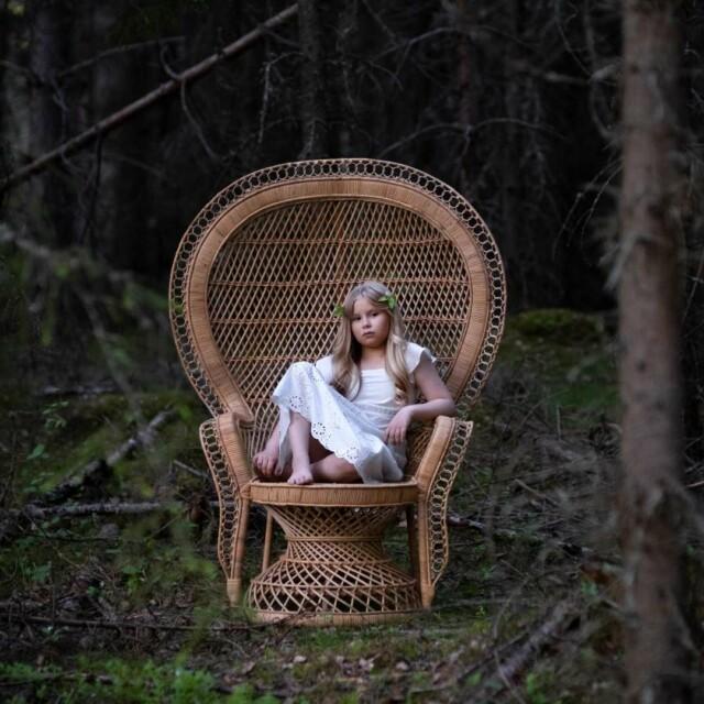 Tyttö istuu Peacock tuolissa keskellä metsää